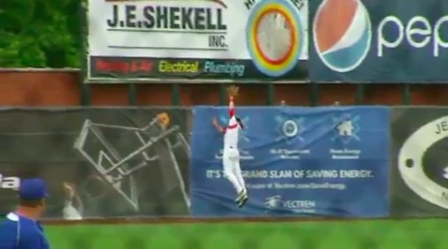 Josh Heuck of Evansville Mater Dei (IN) will remember this catch for the rest of his life! Heuck runs to the fence, climbs the wall, and takes a home run away.