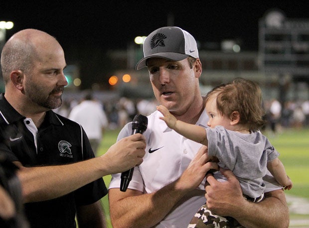 Justin Alumbaugh, holding his eight-month-old son Benicio, goes over the game with the voice of the Spartans, Pat O'Rourke.
