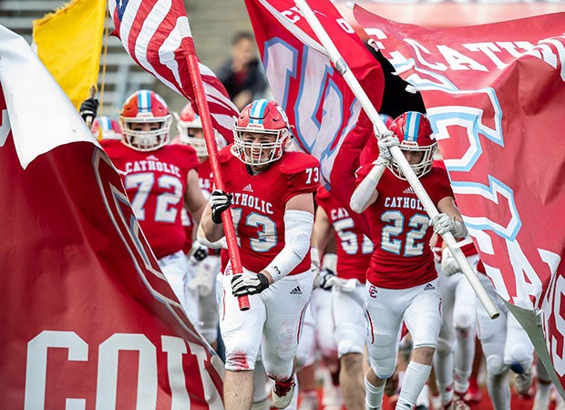 Charlotte Catholic (N.C.) players — led by Matthew Hayek carrying the American flag — bust through a banner while taking the field before the NCHSAA 3A state championship game at Kenan Memorial Stadium at the University of North Carolina.