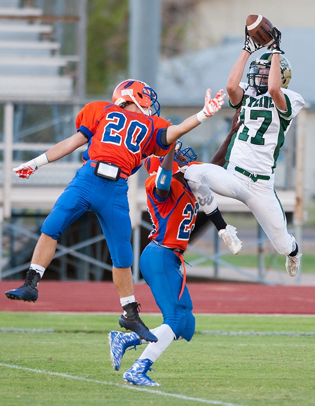 A Skyline (Ariz.) receiver leaps high to make a catch in front of two Westwood defenders during a junior varsity game.