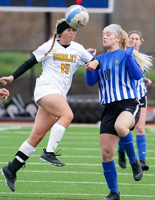 A Godley (Texas) player connects a header in front of a Midlothian defender in a junior varsity game.