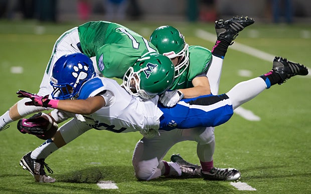 A Bothell (Wash.) ballcarrier dives forward while being pulled down by two Woodinville (Wash.) defenders.