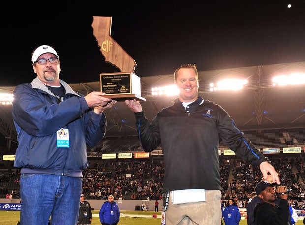 Bakerfield coach Paul Golla holds up the championship plaque following his team's 56-26 win over Del Oro.