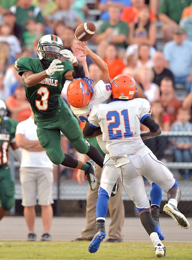 Two Osceola (Fla.) players converge on the ball as a Seminole (Fla.) player leaps.