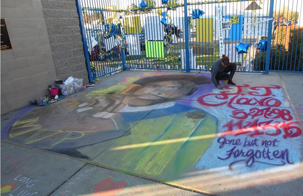 A woman paints a chalk mural on the ground inside the football stadium in tribute to JJ Clavo.