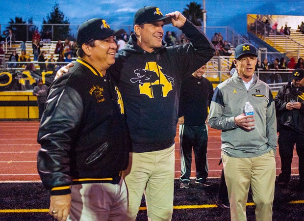 Jim Harbaugh mingles with Antioch principal Louie Rocha during Friday night's game against visiting Liberty.