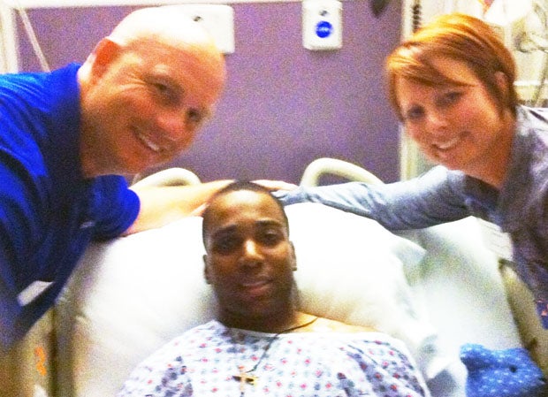 Coach Kelly Davis (left) and his wife Lisa Davis (right) flank Imoter Mngerem at hospital.