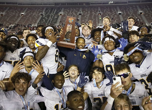 Aquinas head coach Roger Harriott proudly displays the championship trophy while surrounded by his players.