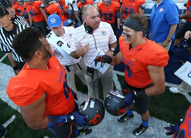 Bishop Gorman coach Tony Sanchez (center) gives instructions to players Nela Otukolo (left) and Nicco Fertitta before the kickoff.