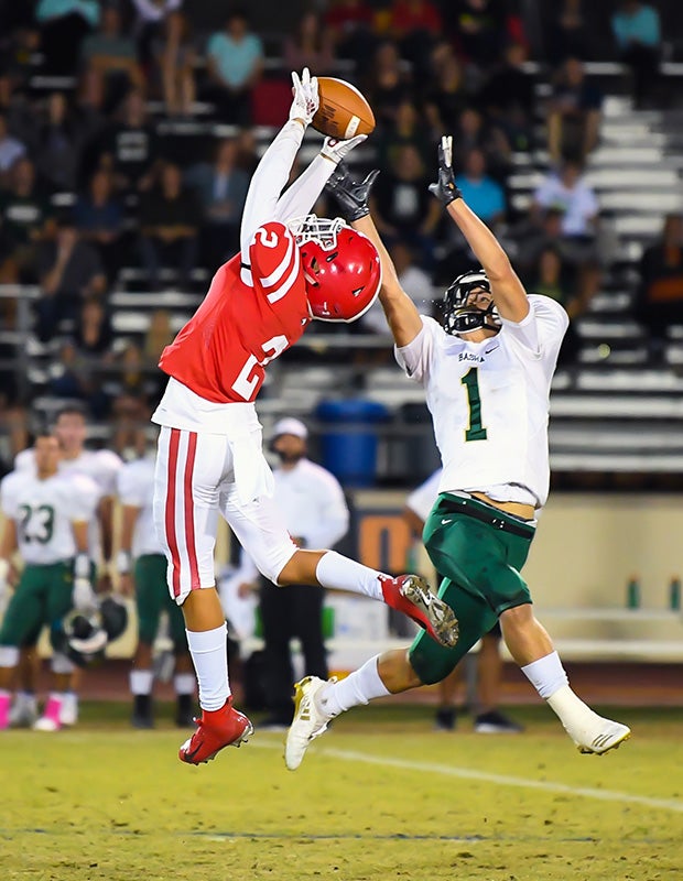 Defensive back Anthony Gonzales of Brophy College Prep (Ariz.) leaps to make an interception in front of Basha athlete Ty Siffermann.