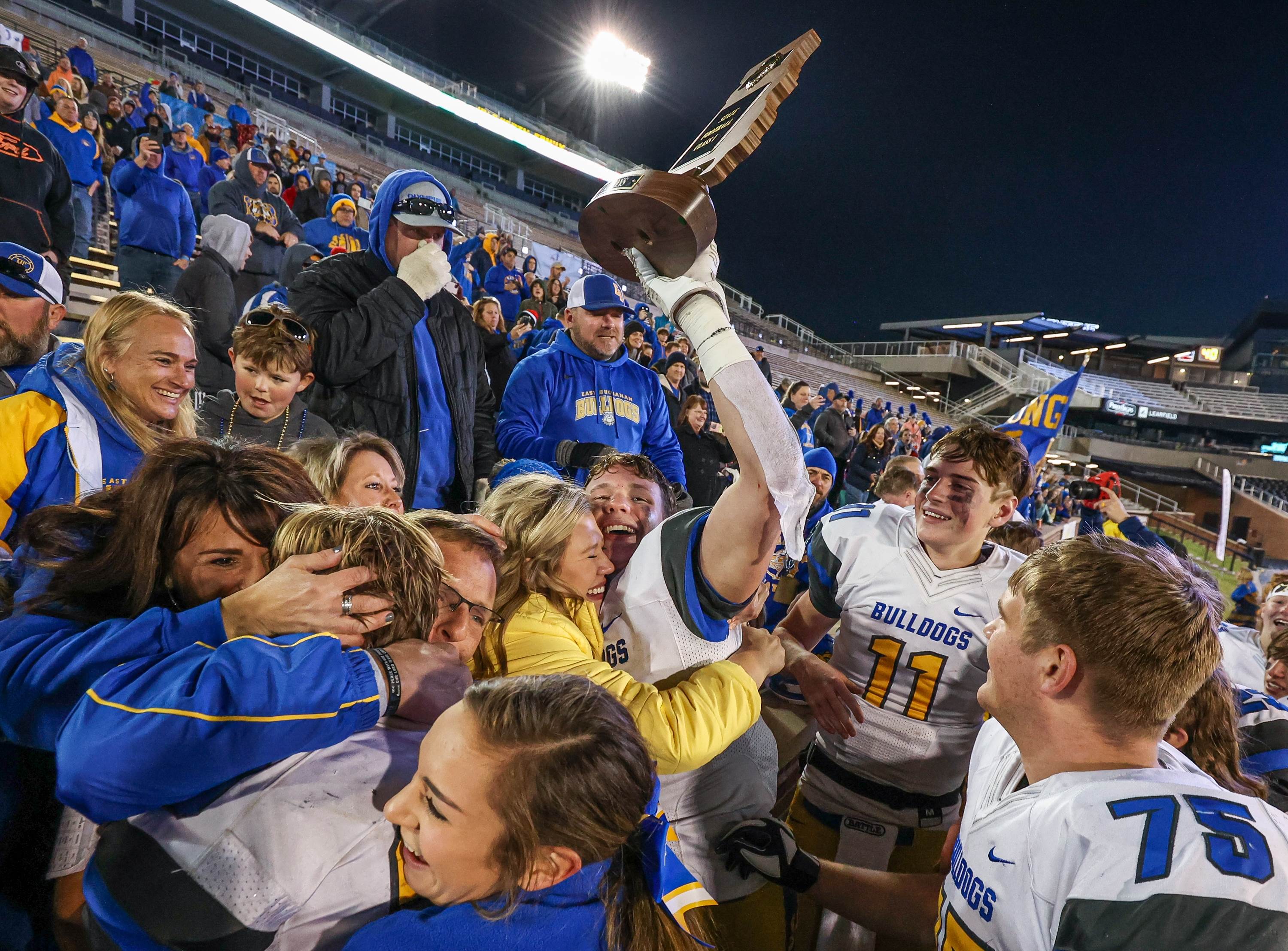 Surrounded by teammates and fans, East Buchanan's Cru Conaway hoists the championship trophy while sharing a hug with his sister, Adlee, following their victory over Marceline in Missouri's Class 1 MSHSAA Show-Me Bowl.