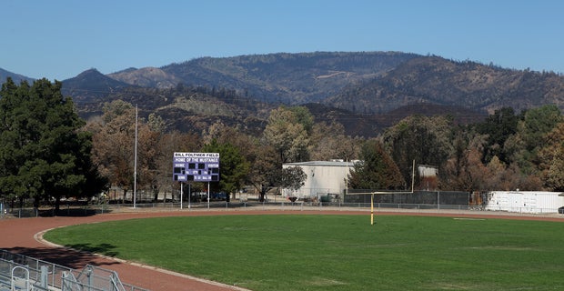 The green field at Bill Foltmer Stadium is in stark contrast to the black, charred hills beyond. 