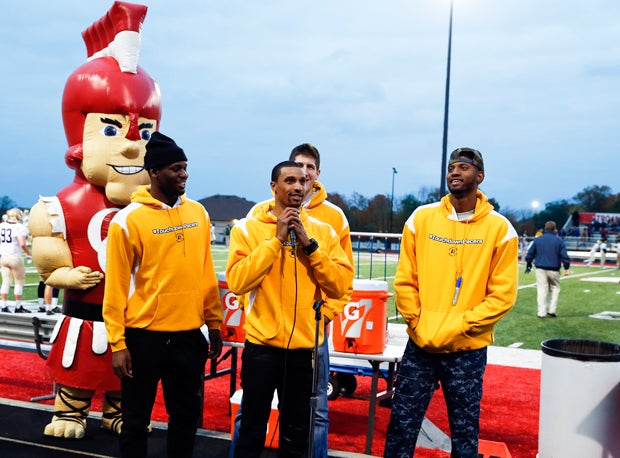 Indiana Pacers player George Hill talks to the fans before the start of the Center Grove vs. Cathedral football game. He is surrounded by teammates Paul George, Damjan Rudez and Adonis Thomas. Center Grove's Trojan mascot is in the background.