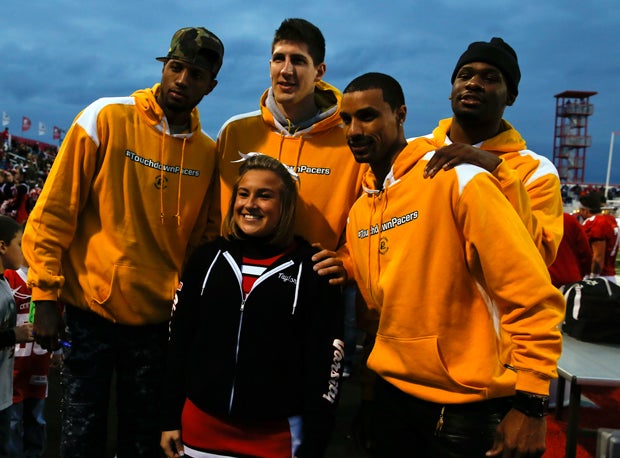 A Center Grove varsity cheerleader poses with Indiana Pacers Paul George, George Hill, Damjan Rudez and Adonis Thomas before the start of the Center Grove vs. Cathedral football game.