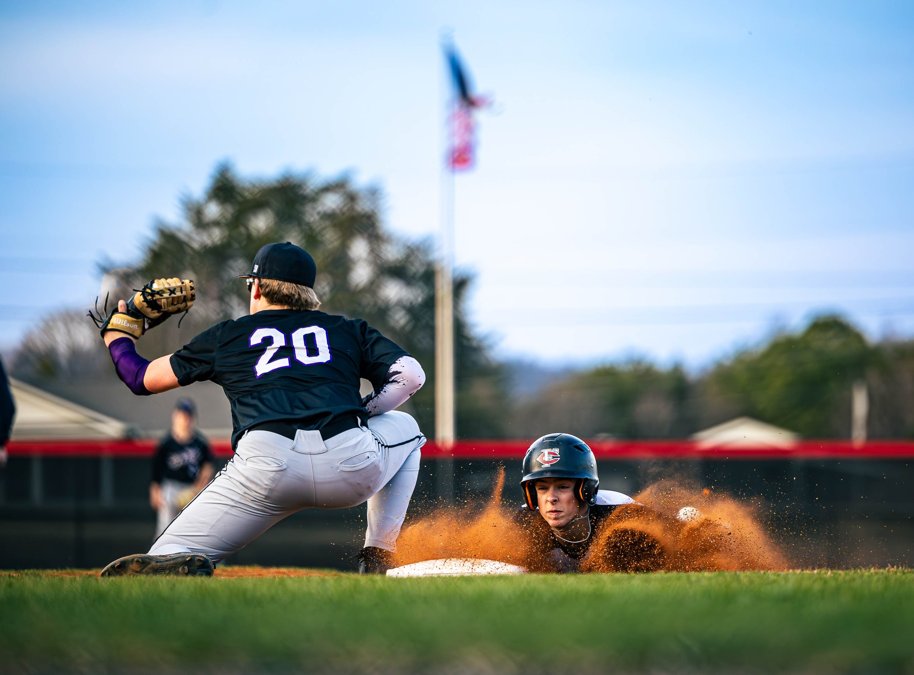 A runner dives back into a cloud of dirt on a pickoff move. (Photo: Chris Meeks)