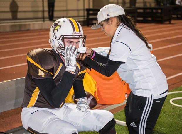 Team manager Beca Perez works on the helmet of Riley Quinn before the team's WCAL finale with St. Ignatius. 