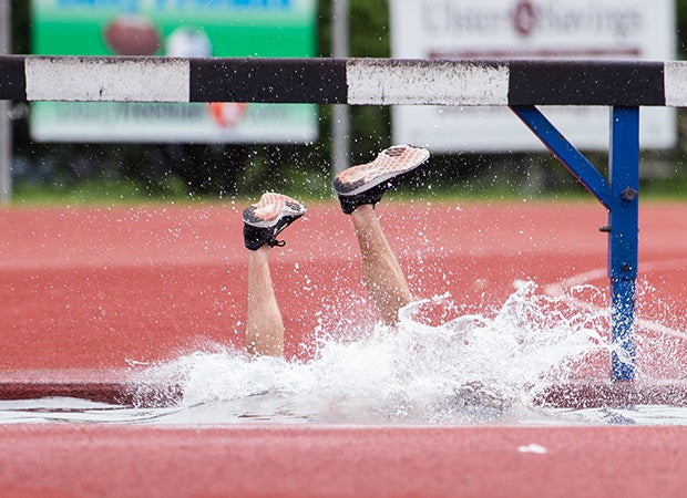 A John Jay (Hopewell Junction, N.Y.) steelechase runner enters the water hazard awkwardly after tripping on the barrier during the Kingston Tiger Relays in New York.
