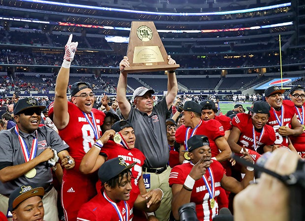 North Shore head coach Jon Kay proudly hoists the trophy as his players celebrate a second straight Texas 6A Division 1 football championship before 47,818 fans at AT&T Stadium. 